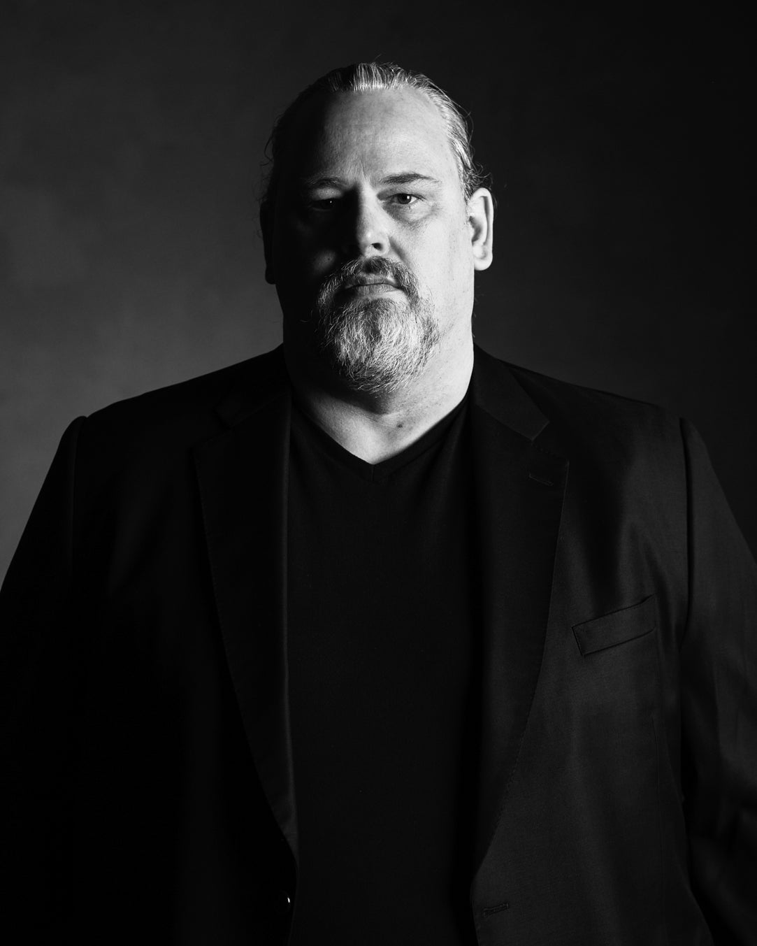 Black and white Portrait of a Middle aged Man with a Gray Goatee Wearing a Black Blazer and Shirt Looking at the Camera
